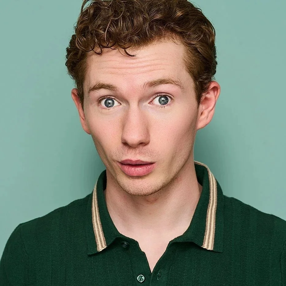 A young man with curly brown hair, blue eyes, and light skin, wearing a dark green polo shirt with beige stripes on the collar, looking directly at the camera with a surprised expression, in front of a light green background.