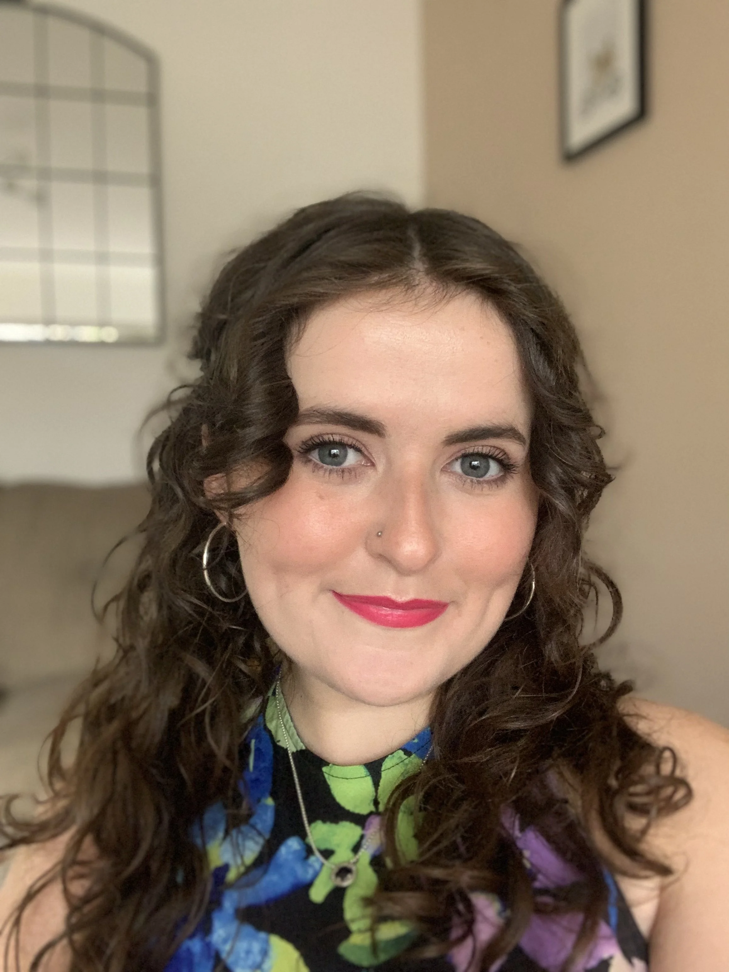 Woman smiling, with brown curly hair, blue eyes, and pink lipstick.