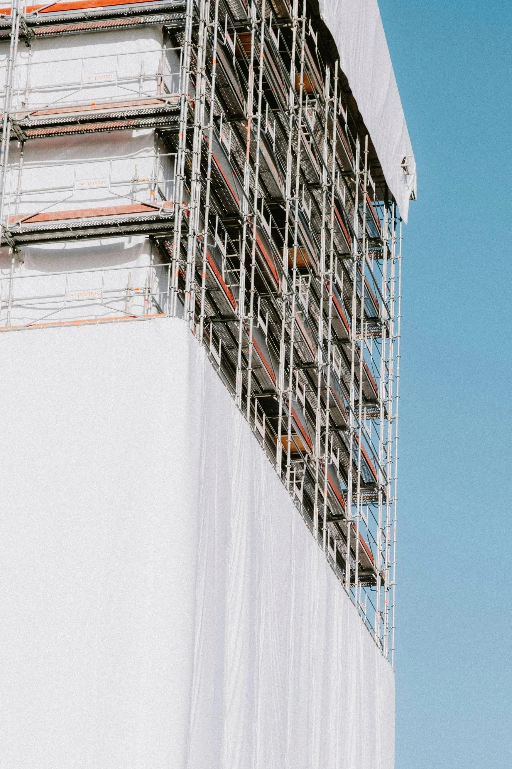 Construction site with scaffolding on a building with a white exterior, against a clear blue sky.