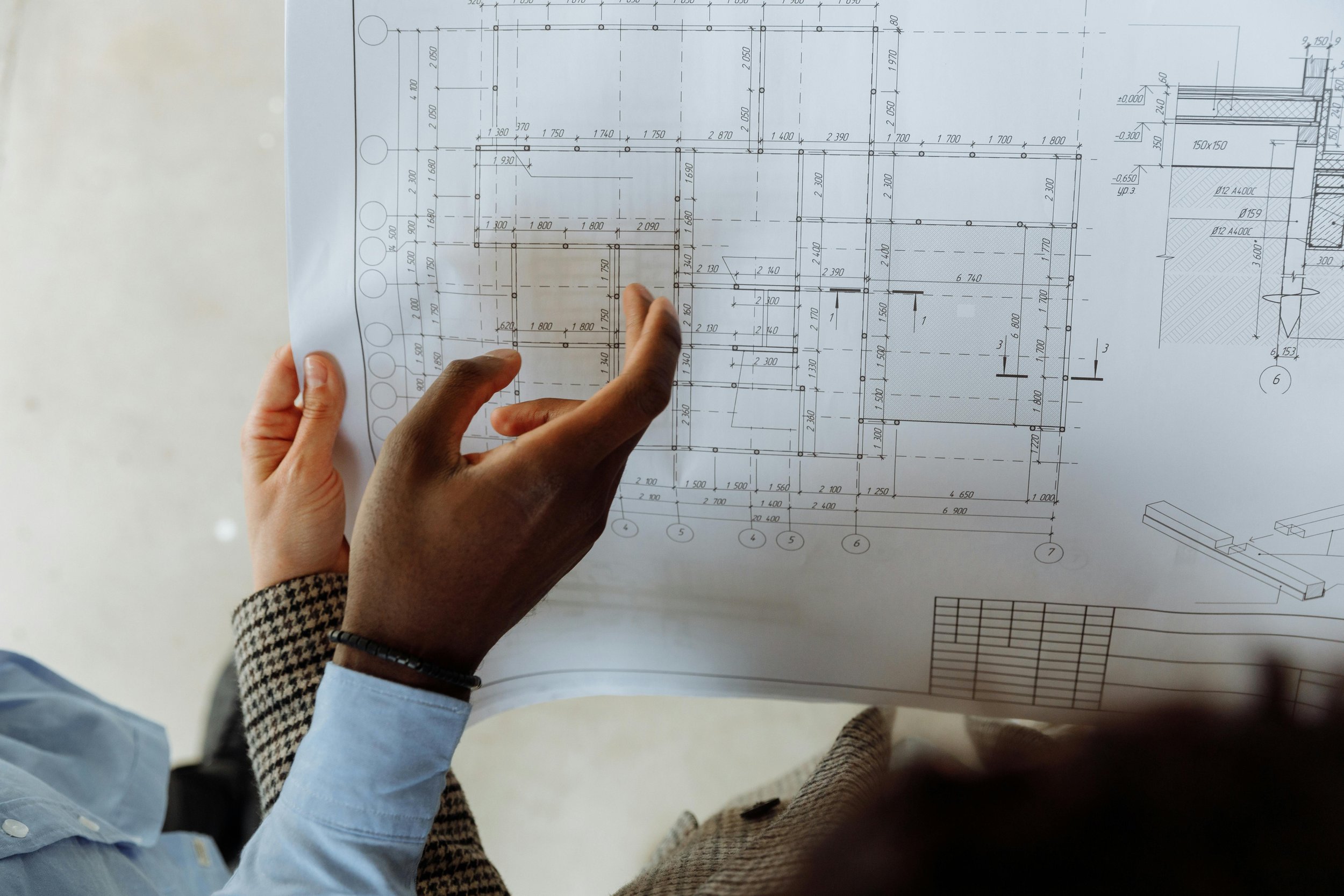 A person pointing at a detailed blueprint or architectural plan on a table, showing various measurements and structural details.