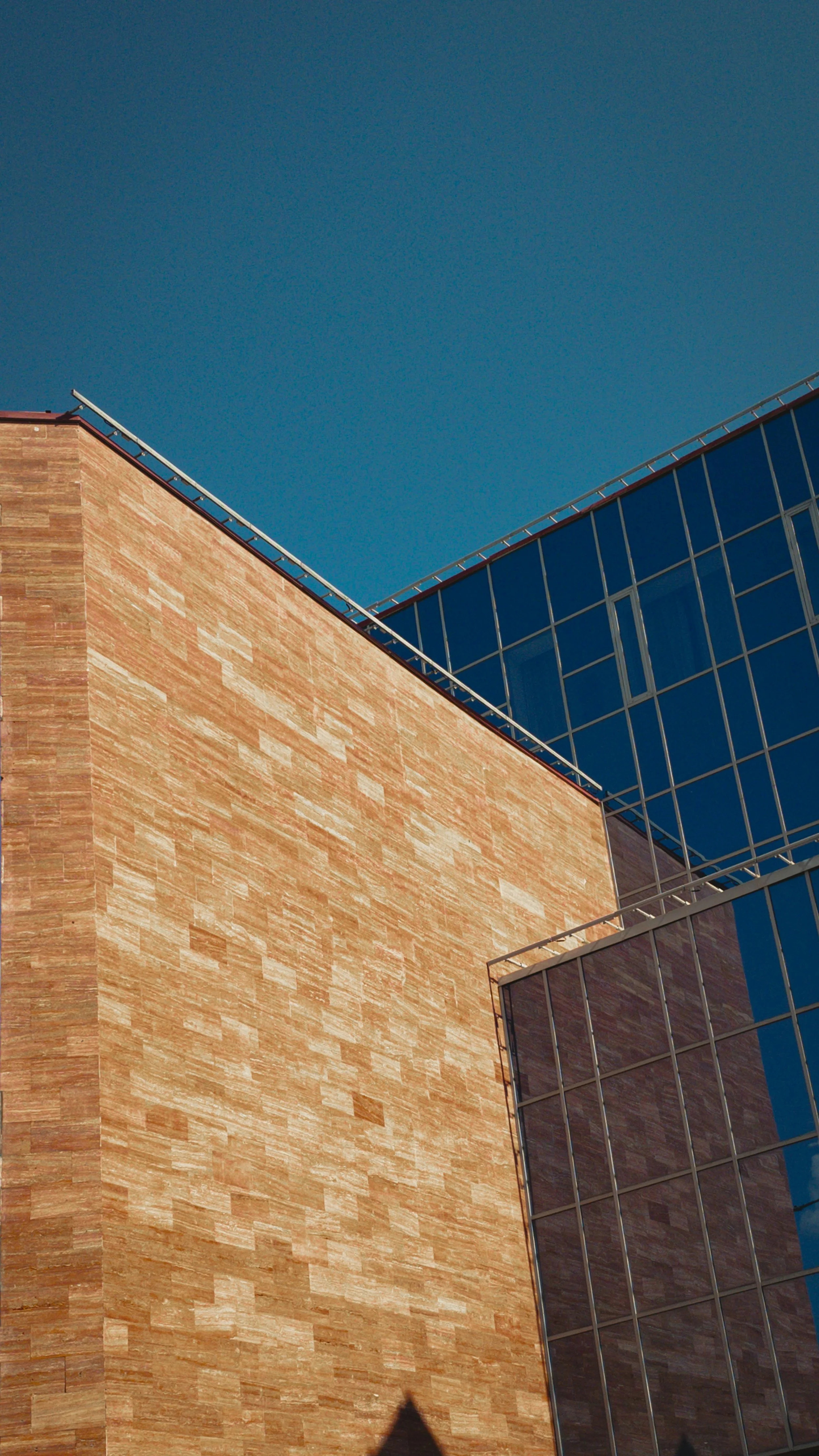 Photo of a modern building with a brick facade and glass windows against a clear blue sky.