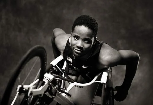 Black and white photo of a male athlete in a wheelchair, looking up at the camera.