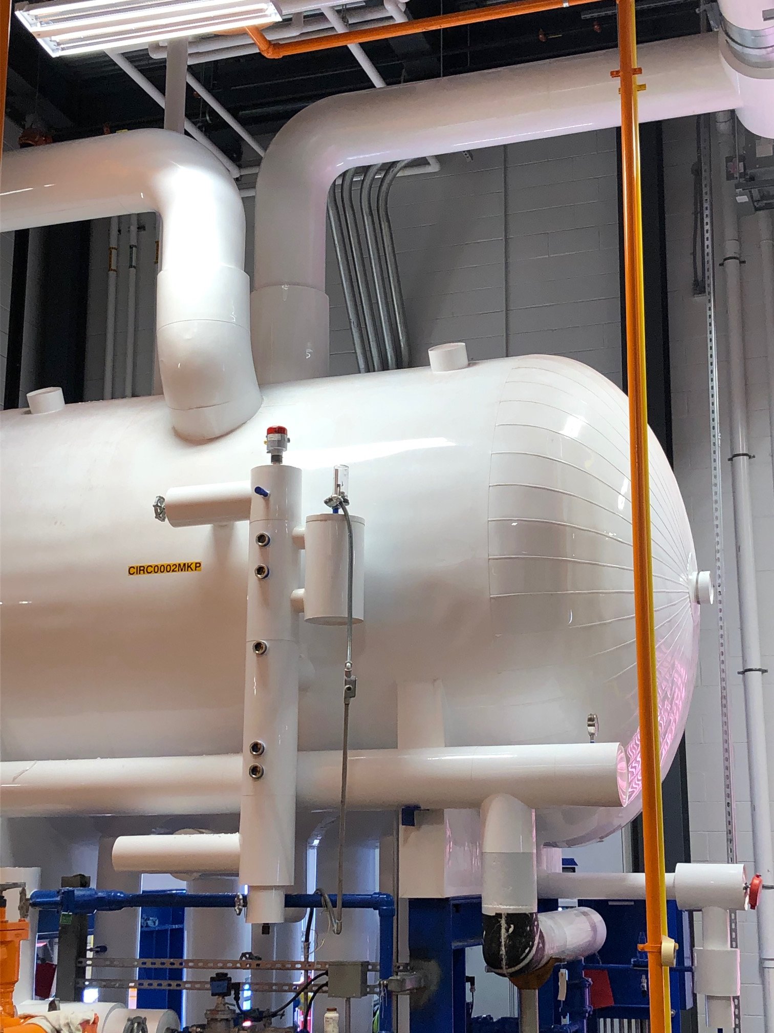 Industrial piping system with large white pipes, valves, and support structures, likely in a factory or power plant