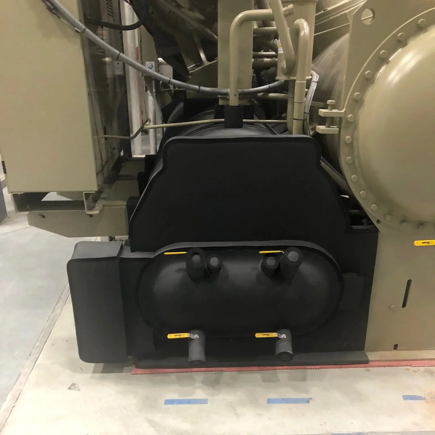 Close-up of an industrial machine or equipment with beige and black components, pipes, and bolts.