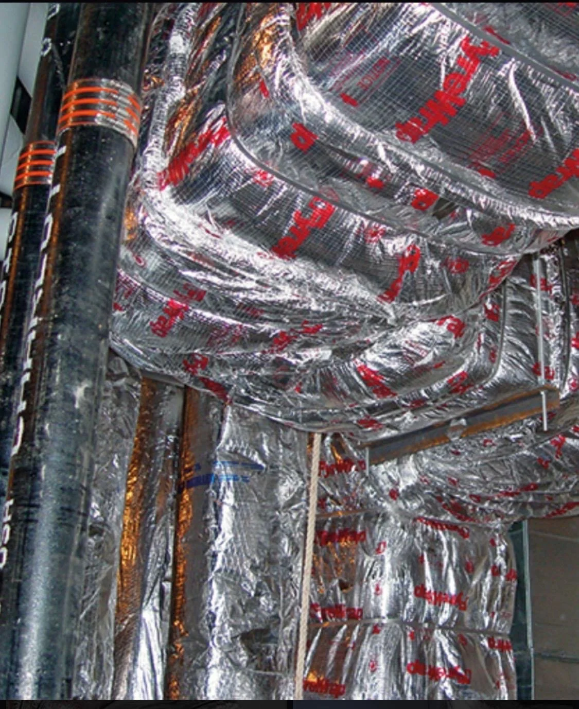Metal HVAC ducts wrapped with insulation material in a construction setting.