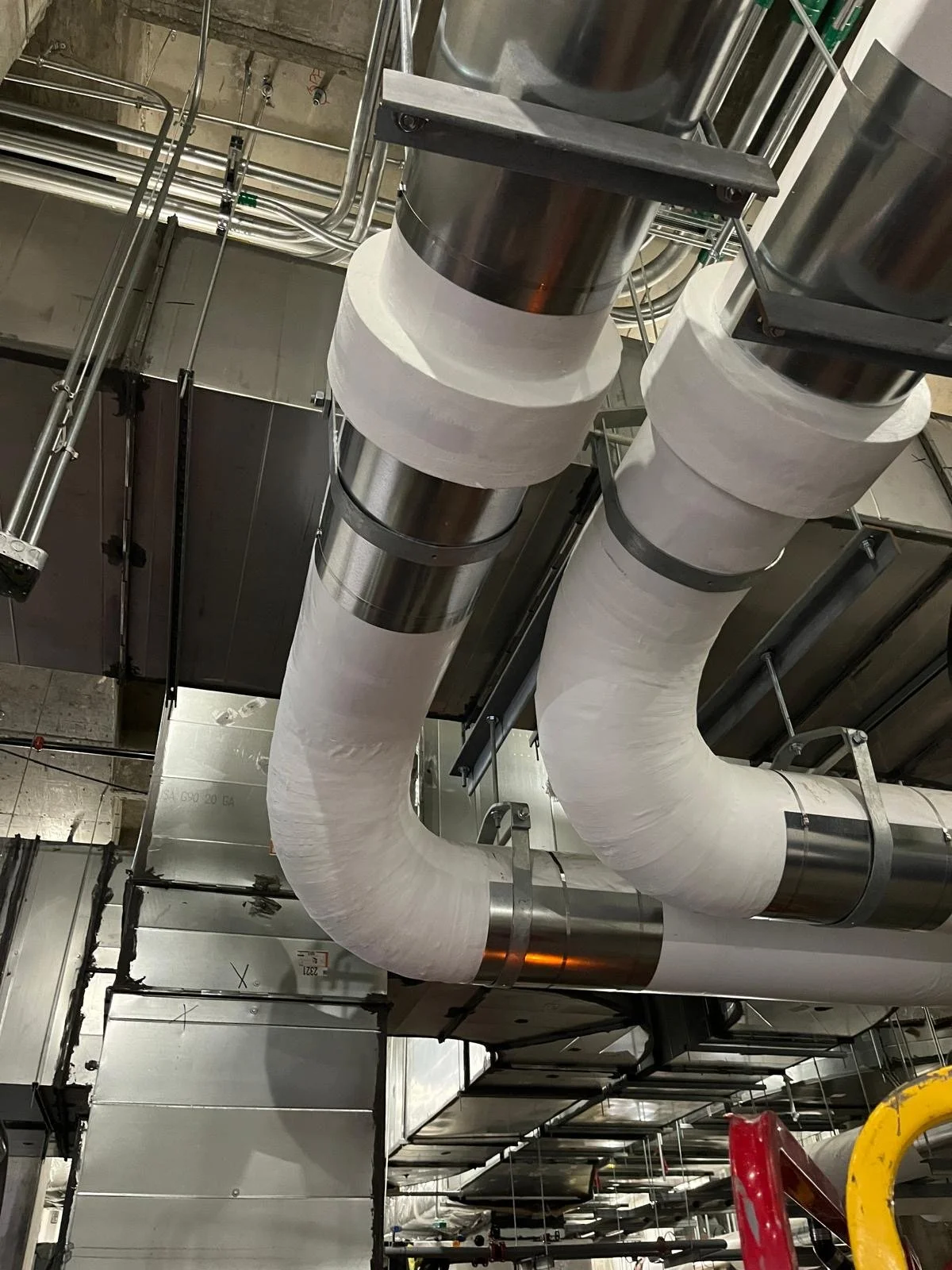 Industrial ductwork and piping system in a building, with insulated pipes and metal supports.
