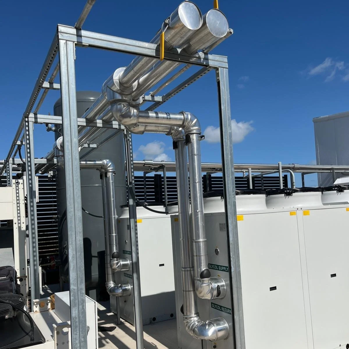Industrial equipment with metal pipes and ducts against a blue sky.