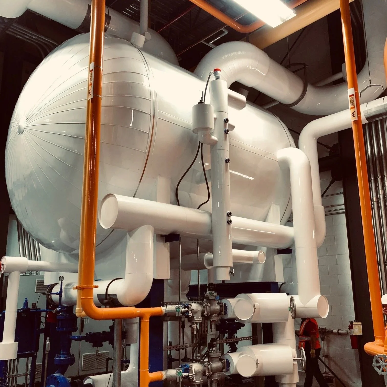 Industrial machinery with white and orange pipes, valves, and large cylindrical tanks.