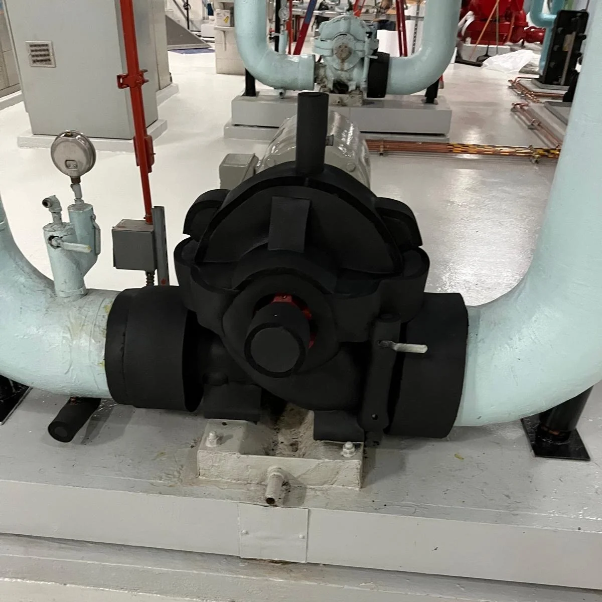 Large industrial pipes connected with hydraulic or pneumatic fittings in a mechanical room or plant.