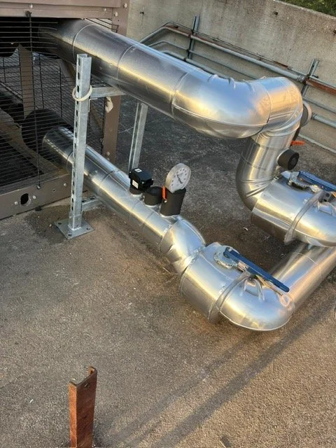 Metal pipes and valves installed on a concrete surface, likely part of an industrial or HVAC system.