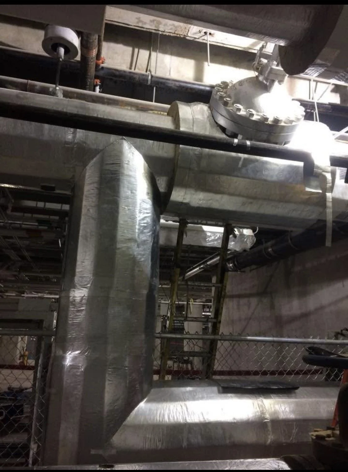 Underground utility room with metal pipes, ducts, and scaffolding.