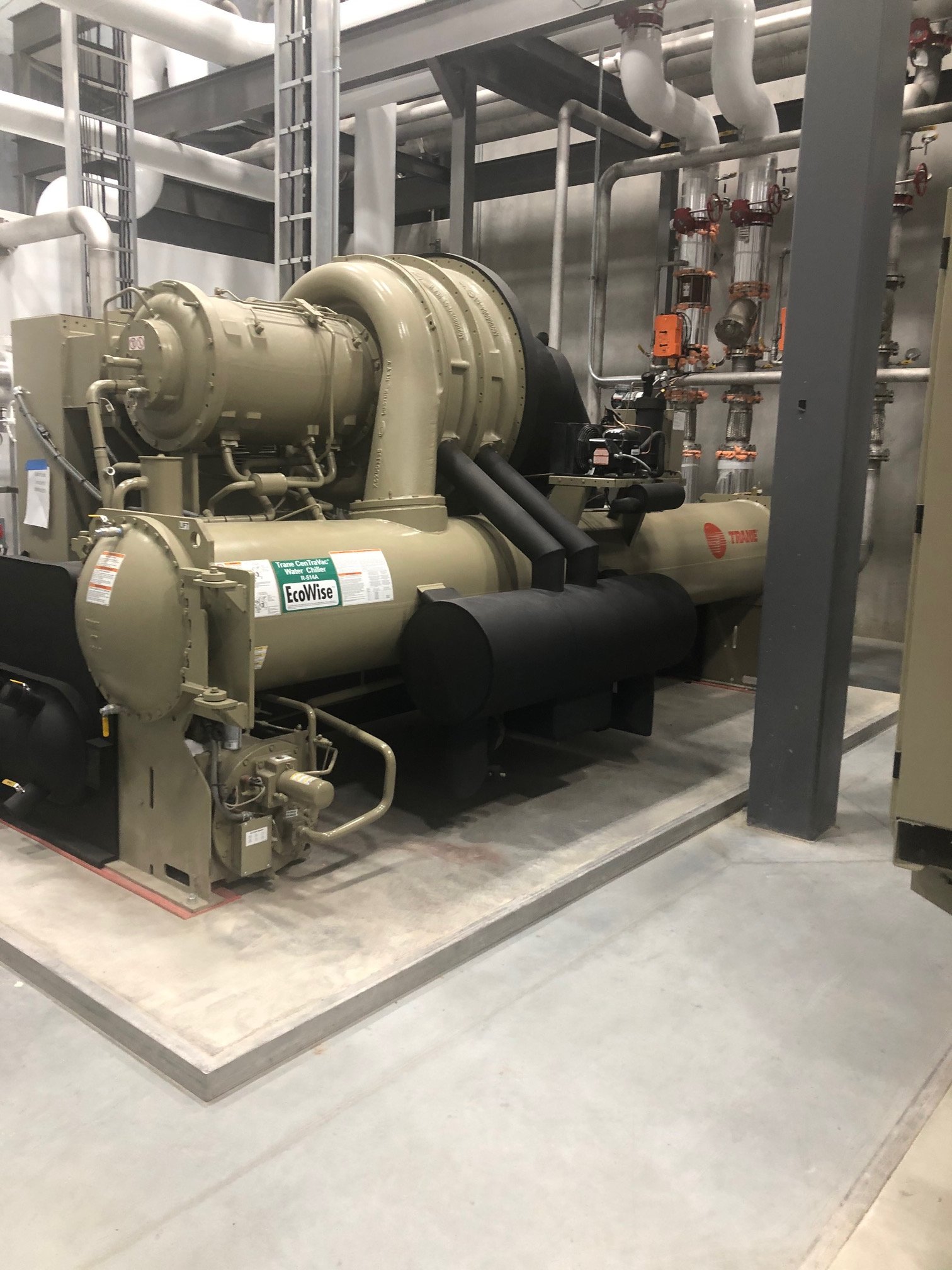Large industrial water chiller machine inside a facility with pipes and valves.