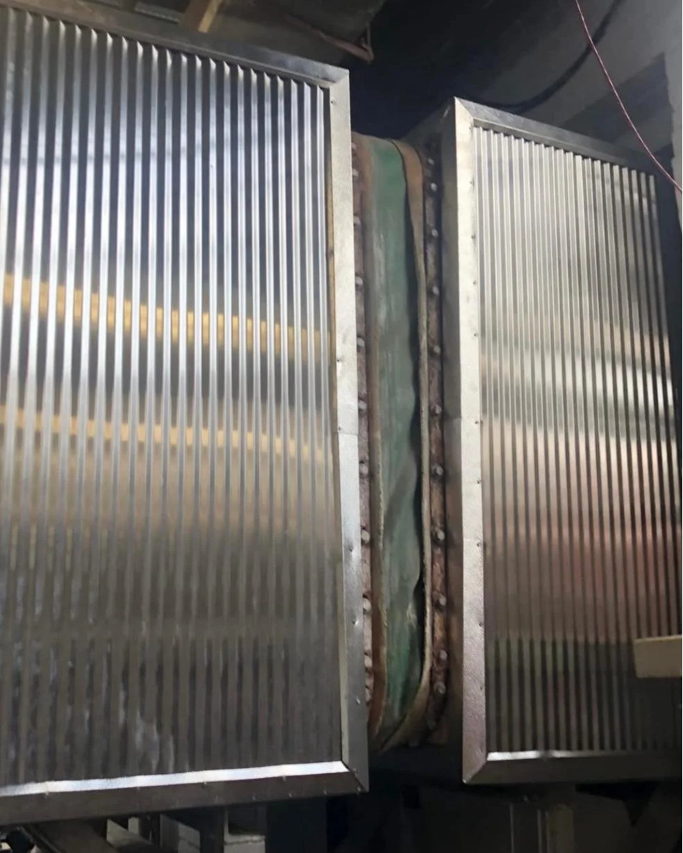 Two metal industrial heat exchangers or radiators with ribbed surfaces, joined together with a metal pipe and bolted connections.