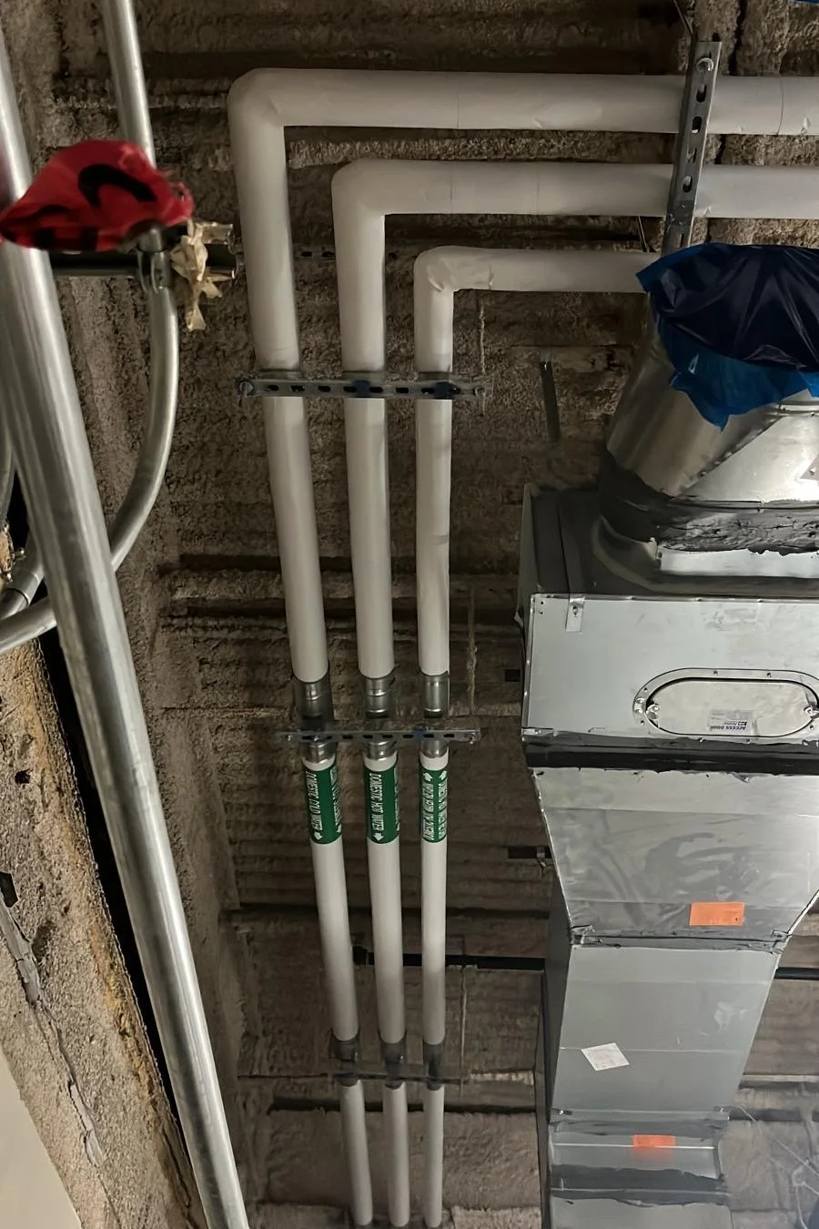 Ceiling with white PVC pipes, ductwork, and metal supports in a building's mechanical room.