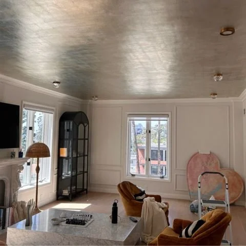 Living room with large windows, a black display cabinet, a floor lamp, and some furniture including chairs and a table.
