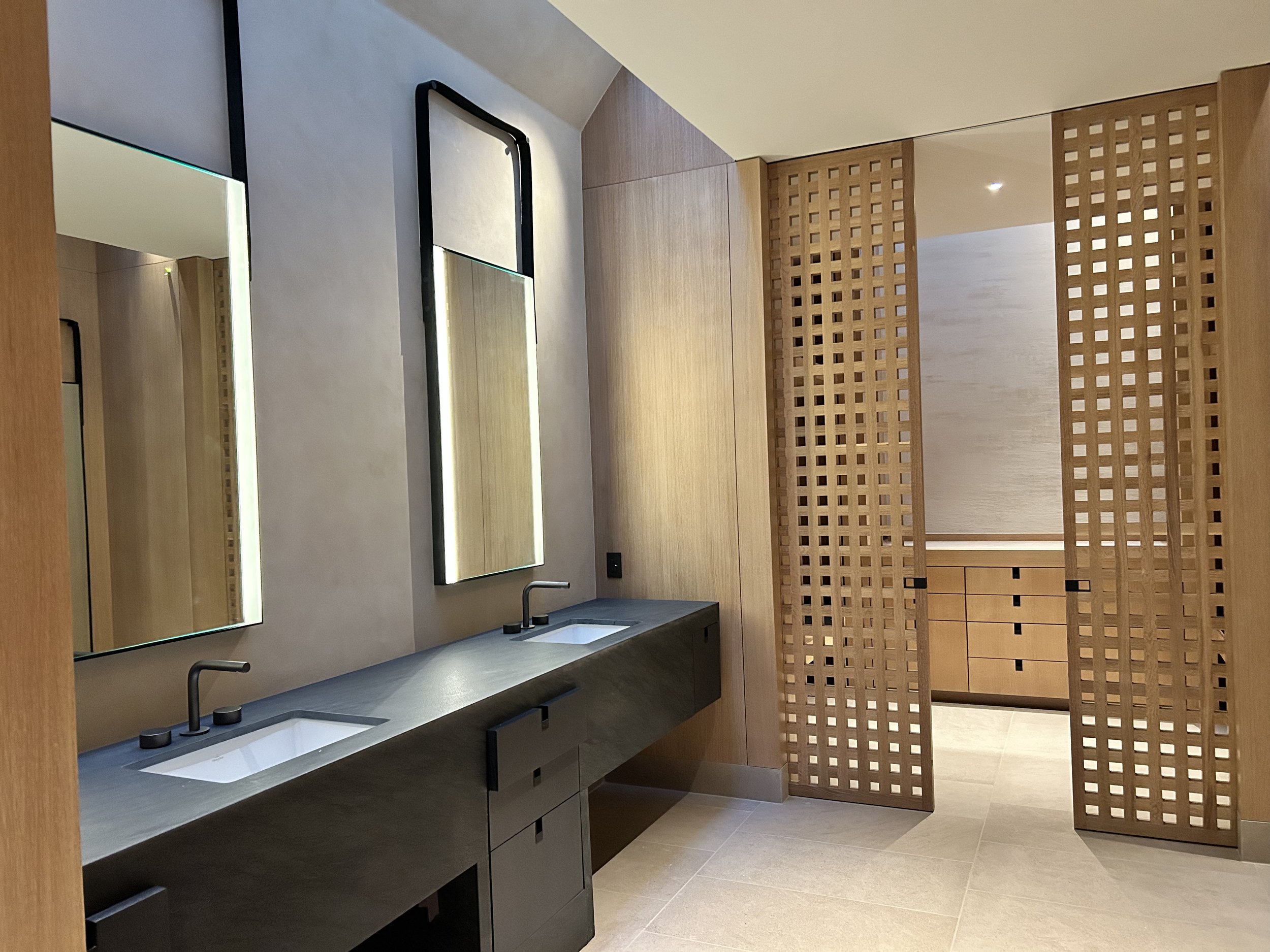Modern bathroom with dual sinks, black faucets, large mirrors, wooden accents, and a privacy lattice.