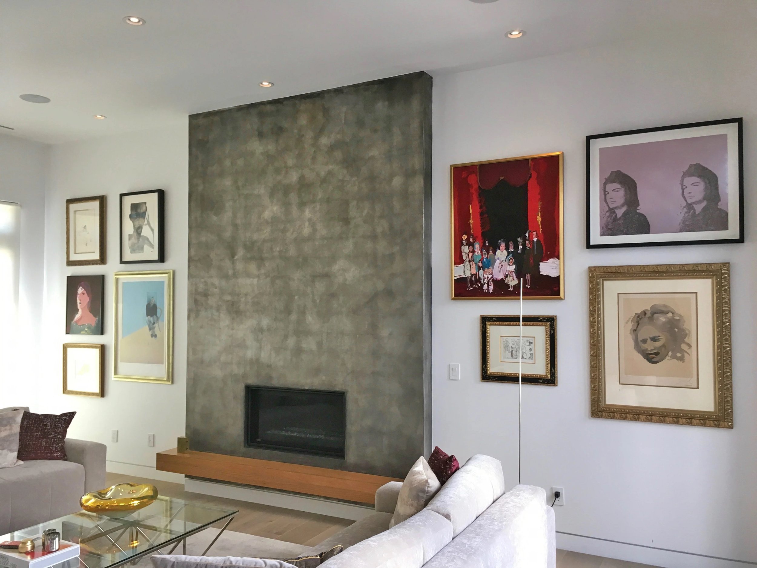 Living room with white walls, white sofas, and an extensive art gallery on the wall including portraits, a group painting, and a Marilyn Monroe print.