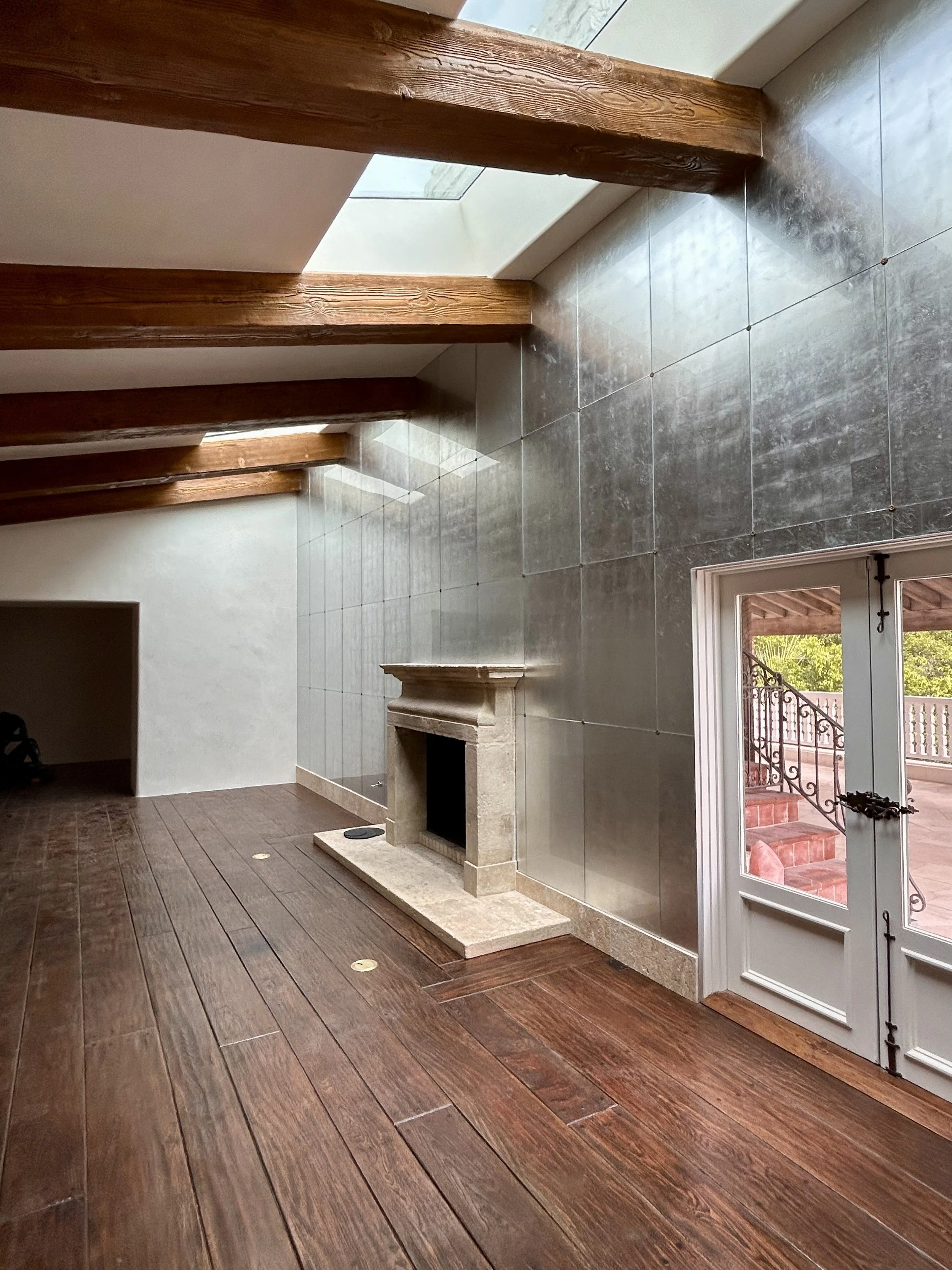 Interior of a room with wooden flooring, a stone fireplace, large windows, and a doorway leading to an outdoor staircase.