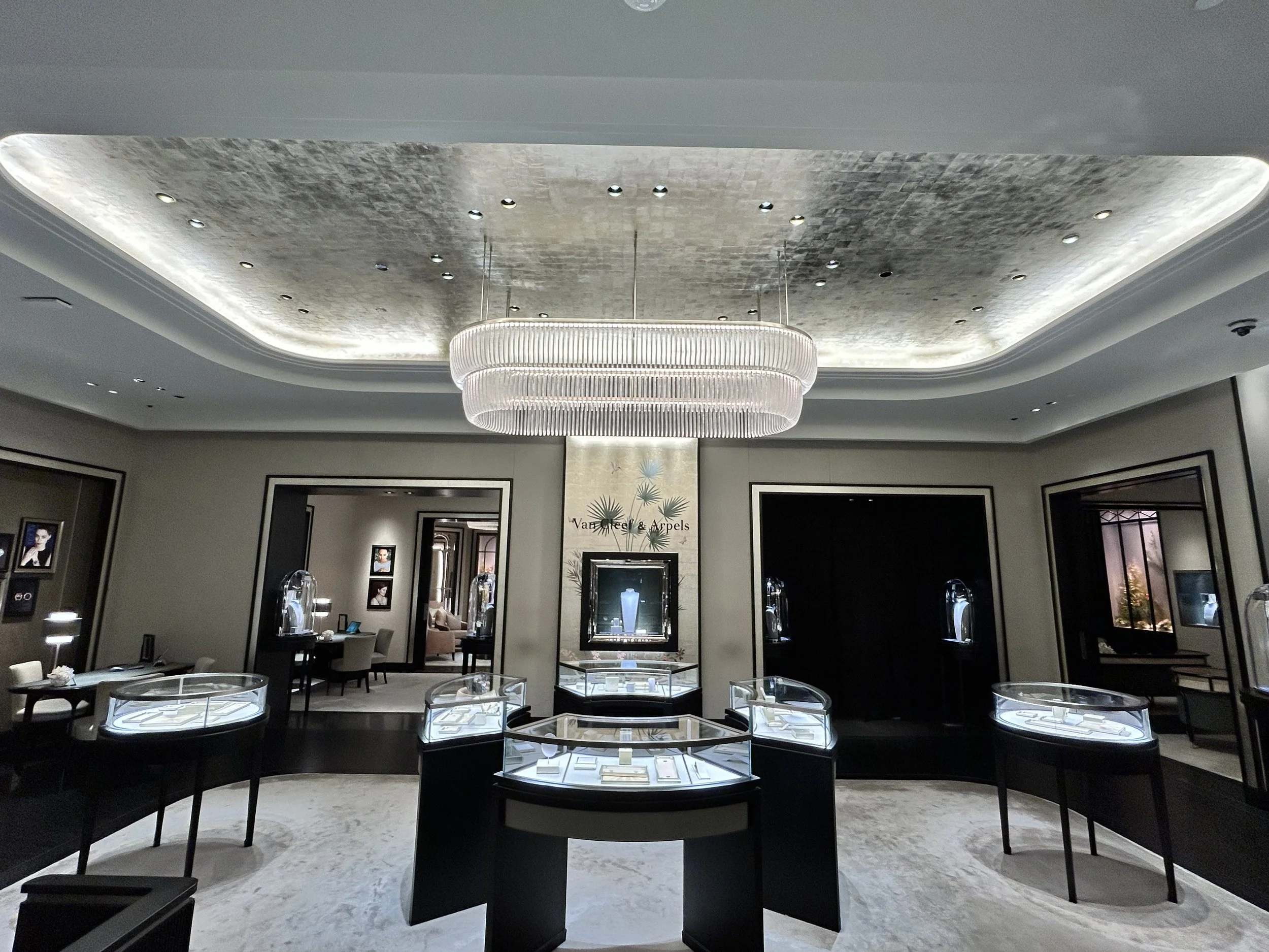 Elegant jewelry store display with glass cases and artwork on the walls, featuring a grand chandelier hanging from a decorative ceiling.
