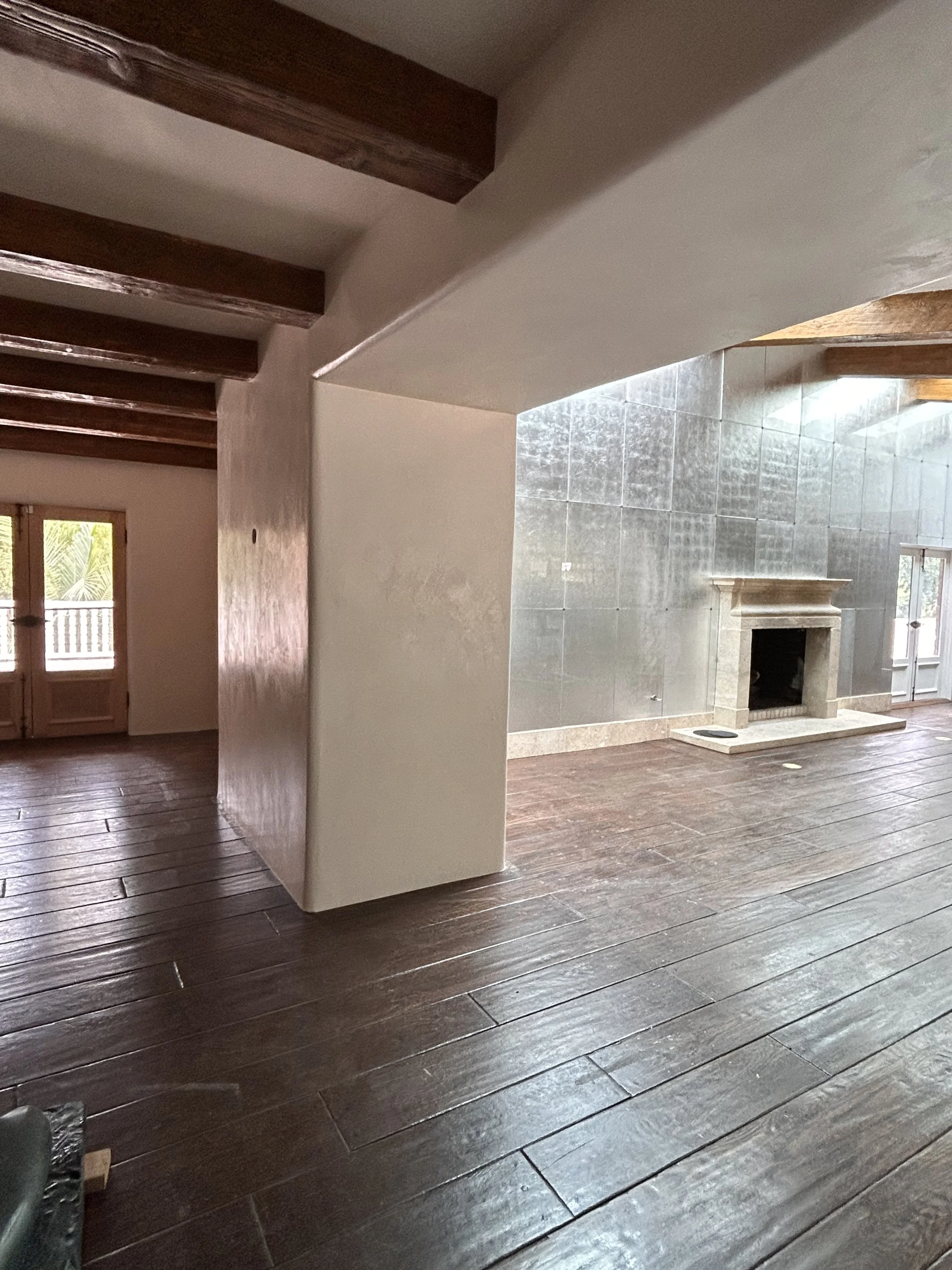 Interior view of a living room with a fireplace, wooden floors, and a corner of a white wall, with a door and window providing natural light.