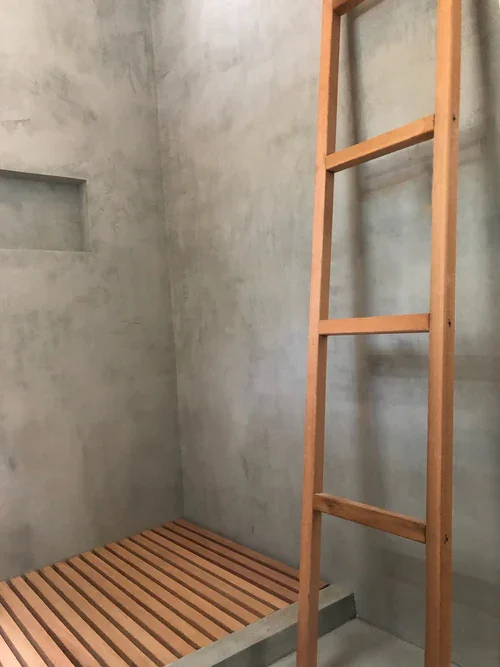Wooden ladder leaning against a concrete wall in a minimalist, unfinished room.