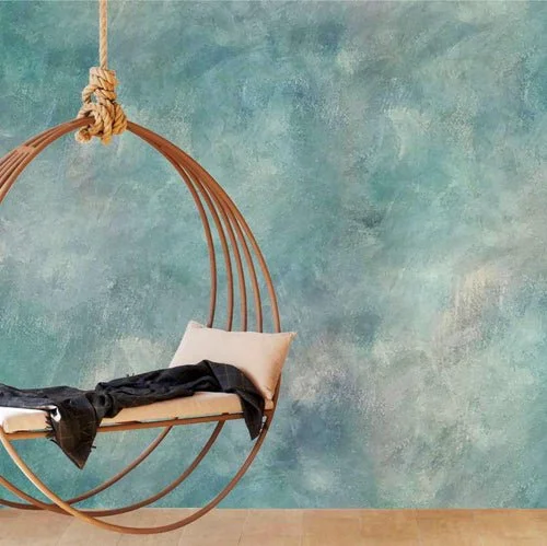 A hanging chair with a pillow, a black jacket, and attached to a rope against a textured blue-green wall.