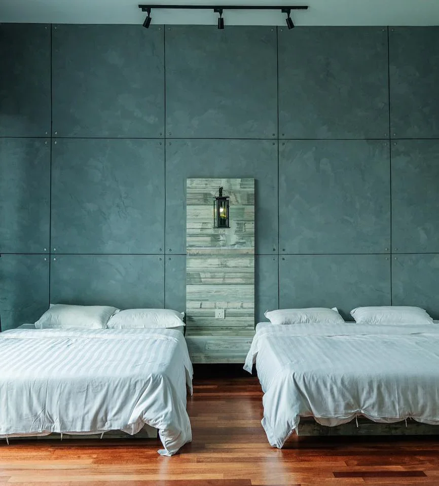 Two neatly made beds with white linens in a modern bedroom with a wooden floor and a blue-green textured wall