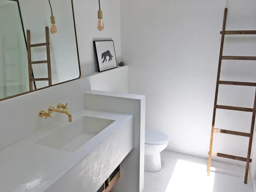 Minimalist bathroom with a white sink, round mirror, framed bear picture, and wooden ladder next to the toilet.