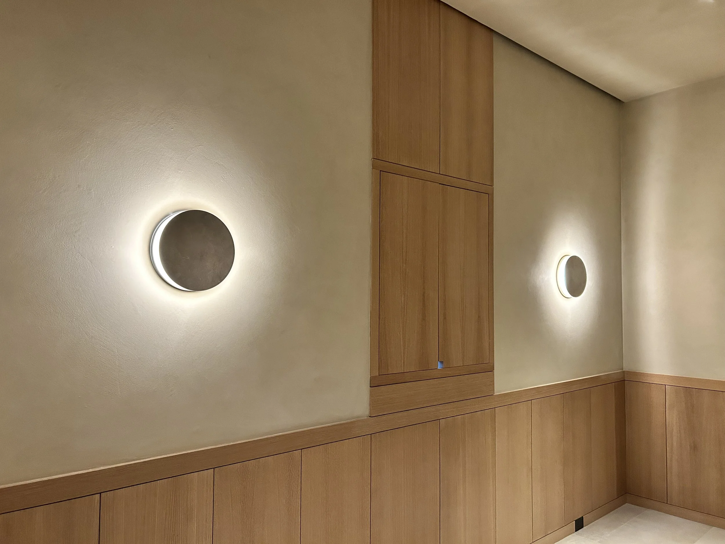 A portion of a room wall with two round wall-mounted lights and a wooden built-in cabinet or closet.