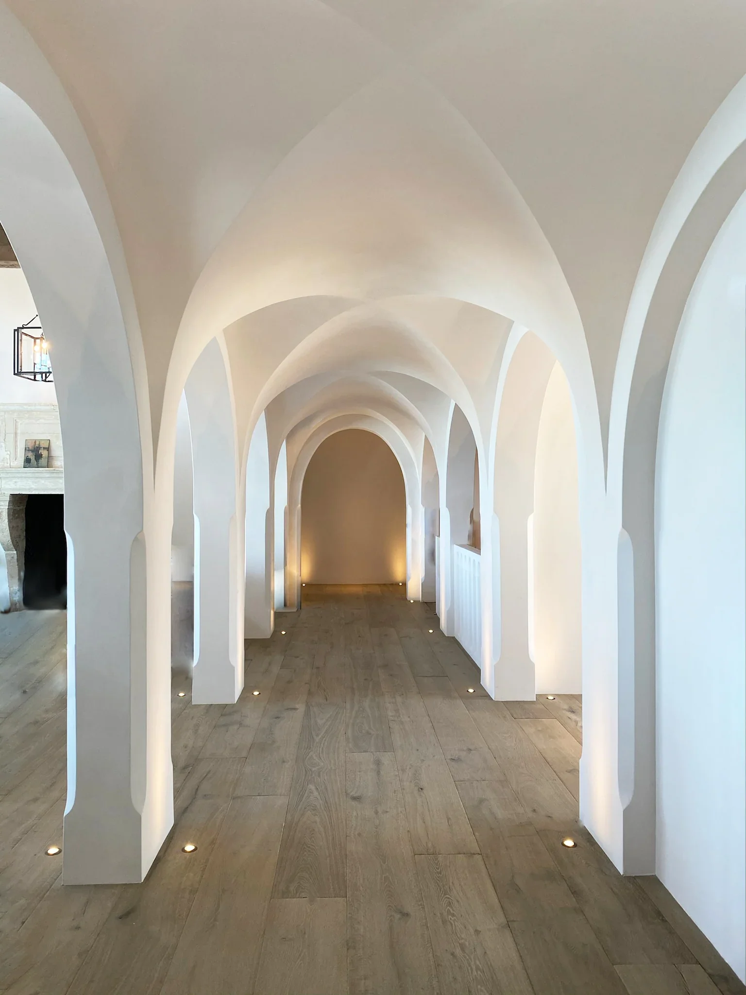 White arched corridor with wooden flooring, subtle lighting, and modern minimalist design.