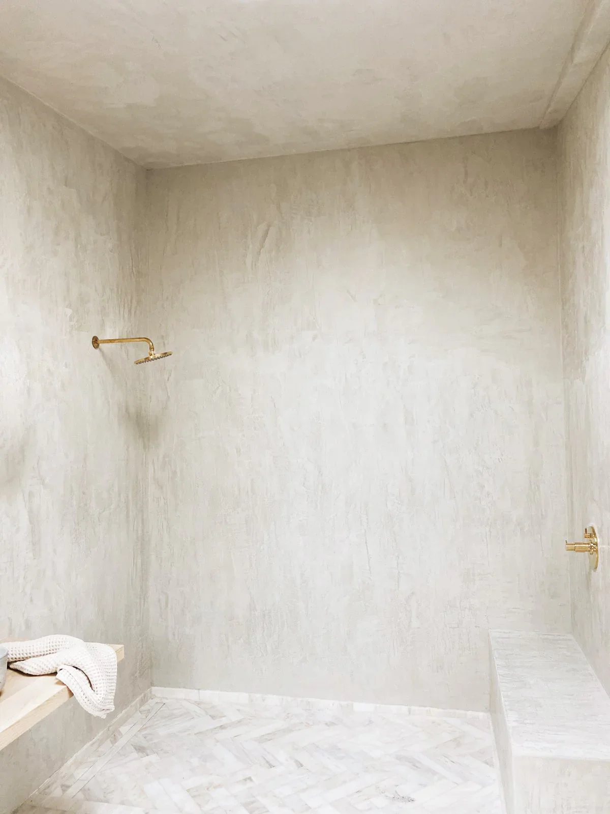 Empty walk-in shower with gold fixtures and beige textured walls.