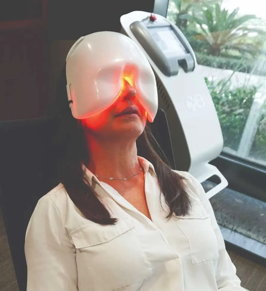 Woman receiving a light therapy facial treatment at a spa or skincare clinic, wearing a facial mask with red light therapy.