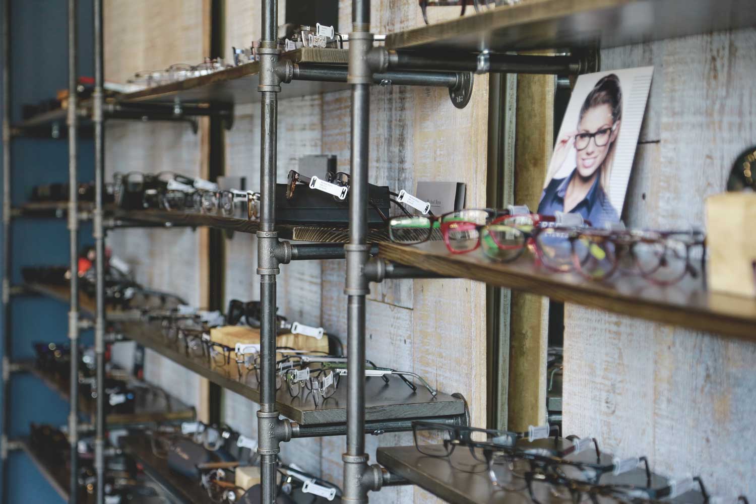 Eyeglasses displayed on shelves with a photograph of a woman wearing glasses in the background.