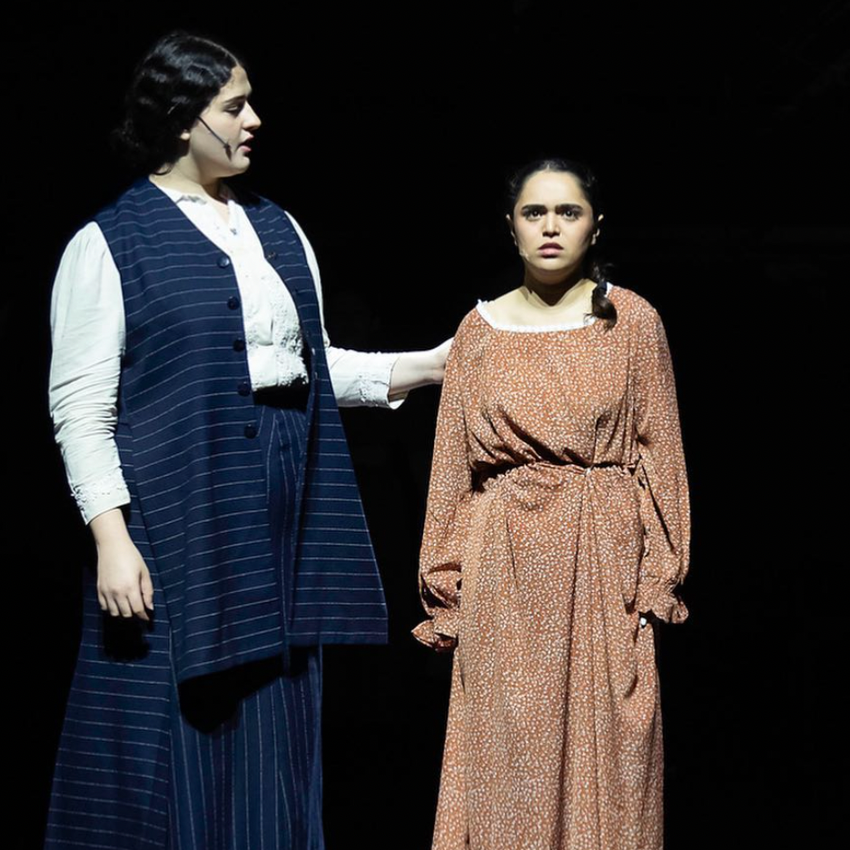 Two women on stage in period costumes, one comforting the other.