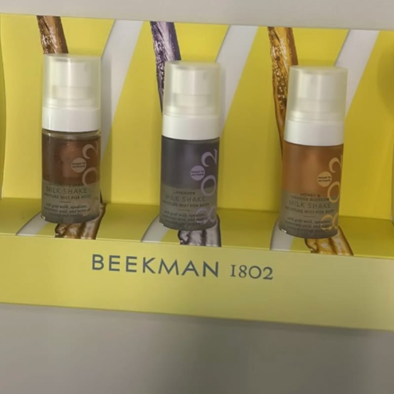 Display of Beekman 1802 Milk Shake skincare bottles in different colors on a yellow shelf.