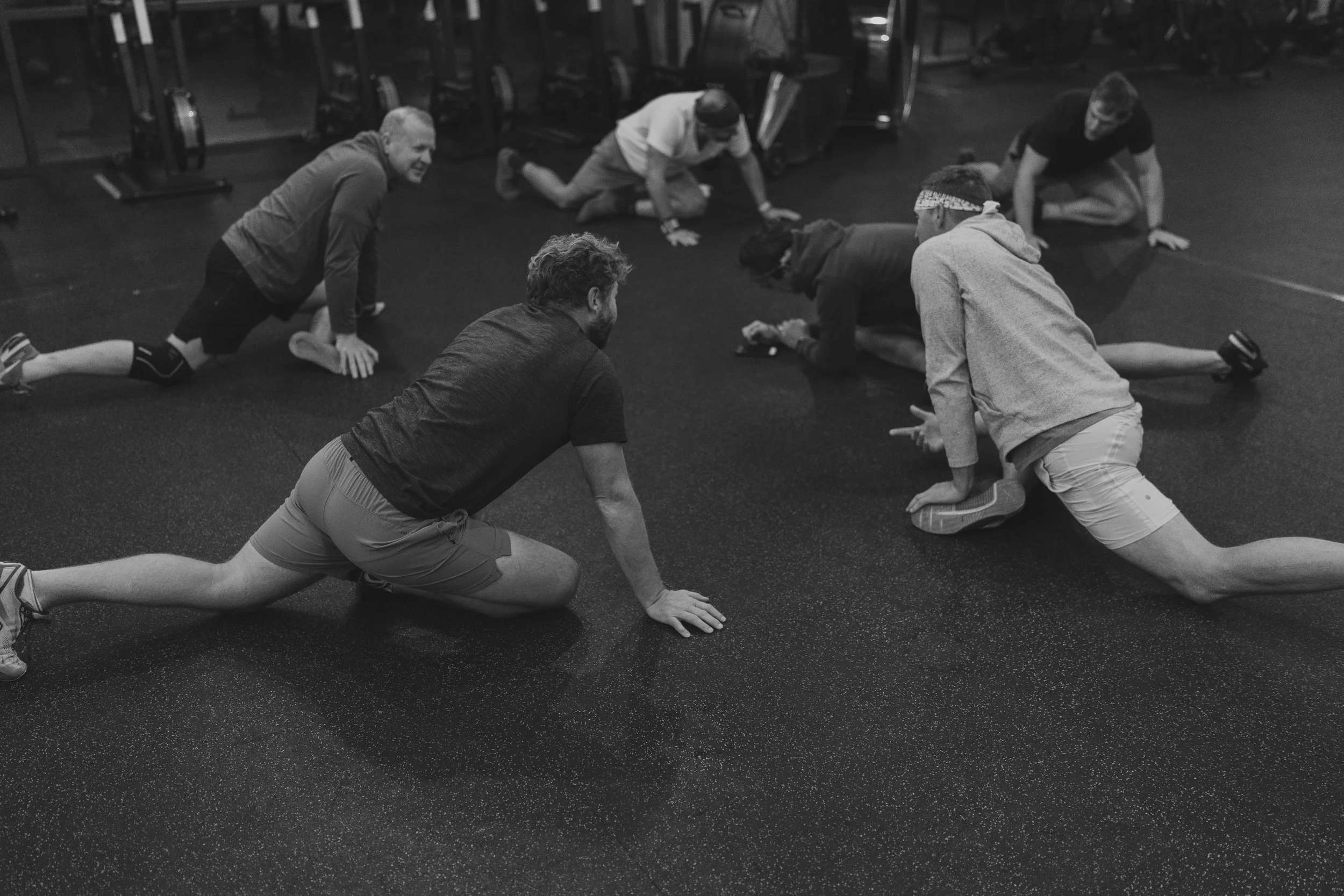 People in a gym doing a group stretch stretch on the ground.