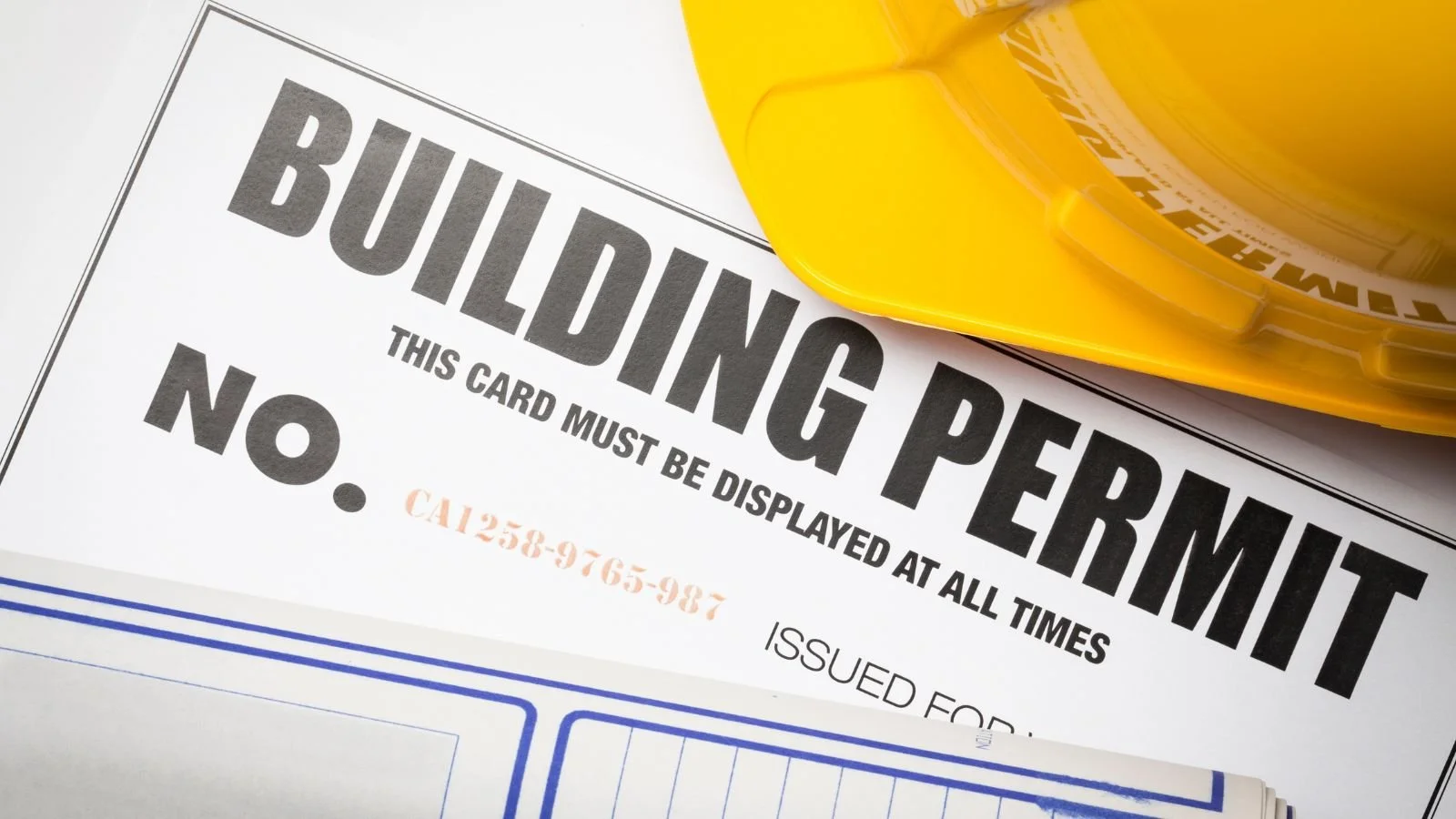 Close-up of a construction permit form and a yellow construction hard hat.