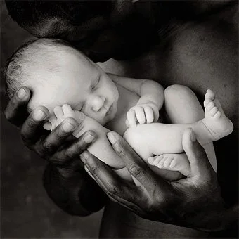 A newborn baby sleeping peacefully while cradled in an adult's hands.