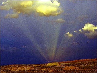 Sunbeams shining through dark clouds over a desert landscape.