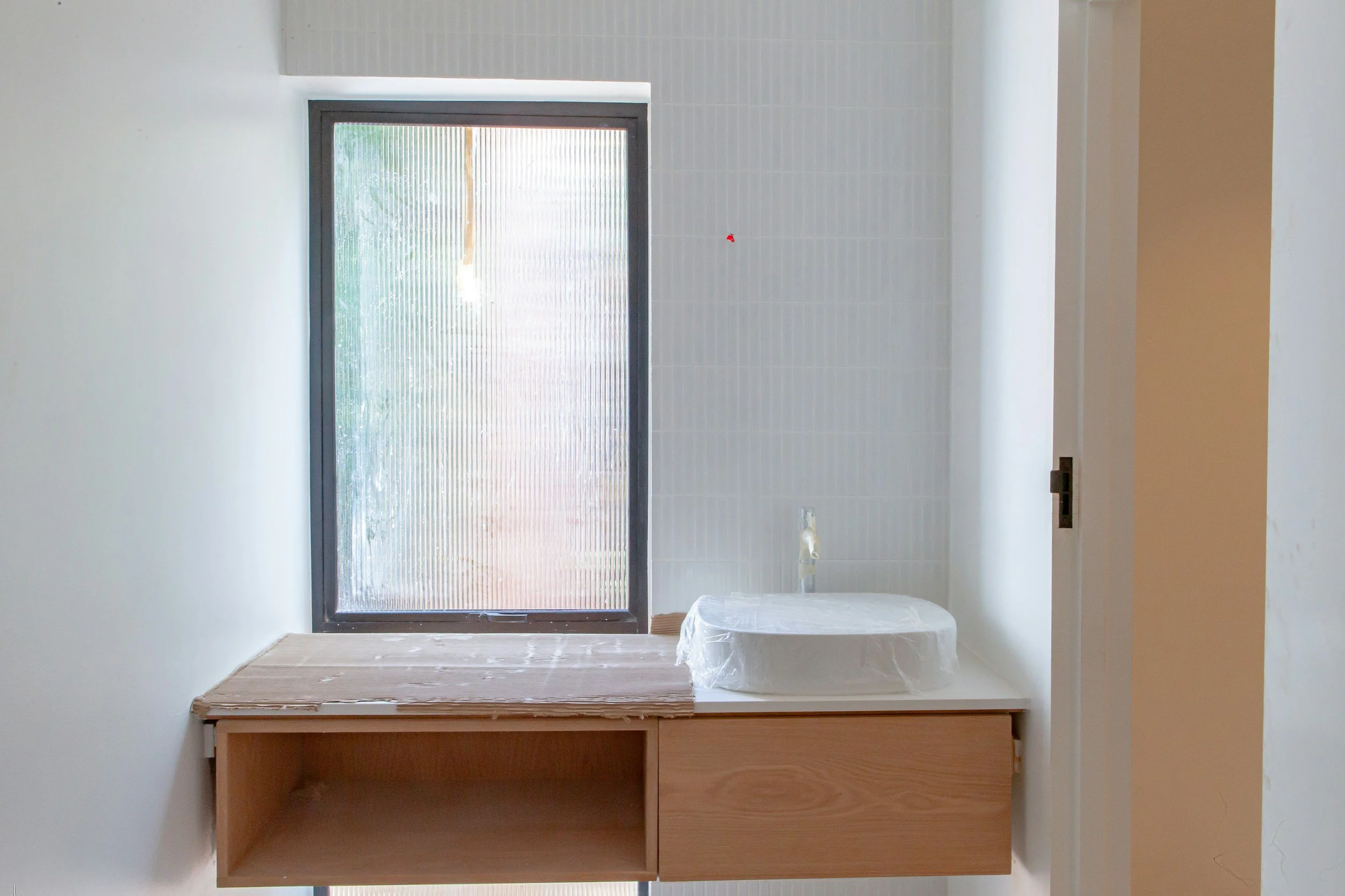 Interior view of a room with a window, a small wooden desk, and a covered object on the floor.