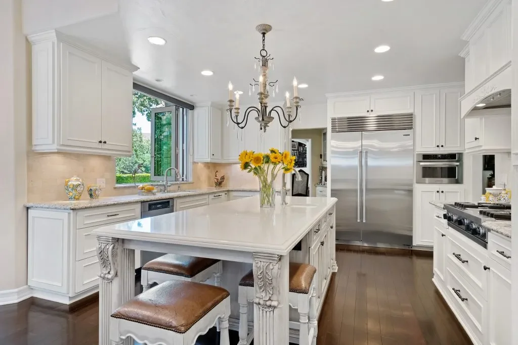 Bright white kitchen with an island, sunflowers in a vase, stainless steel appliances, and hardwood floors.