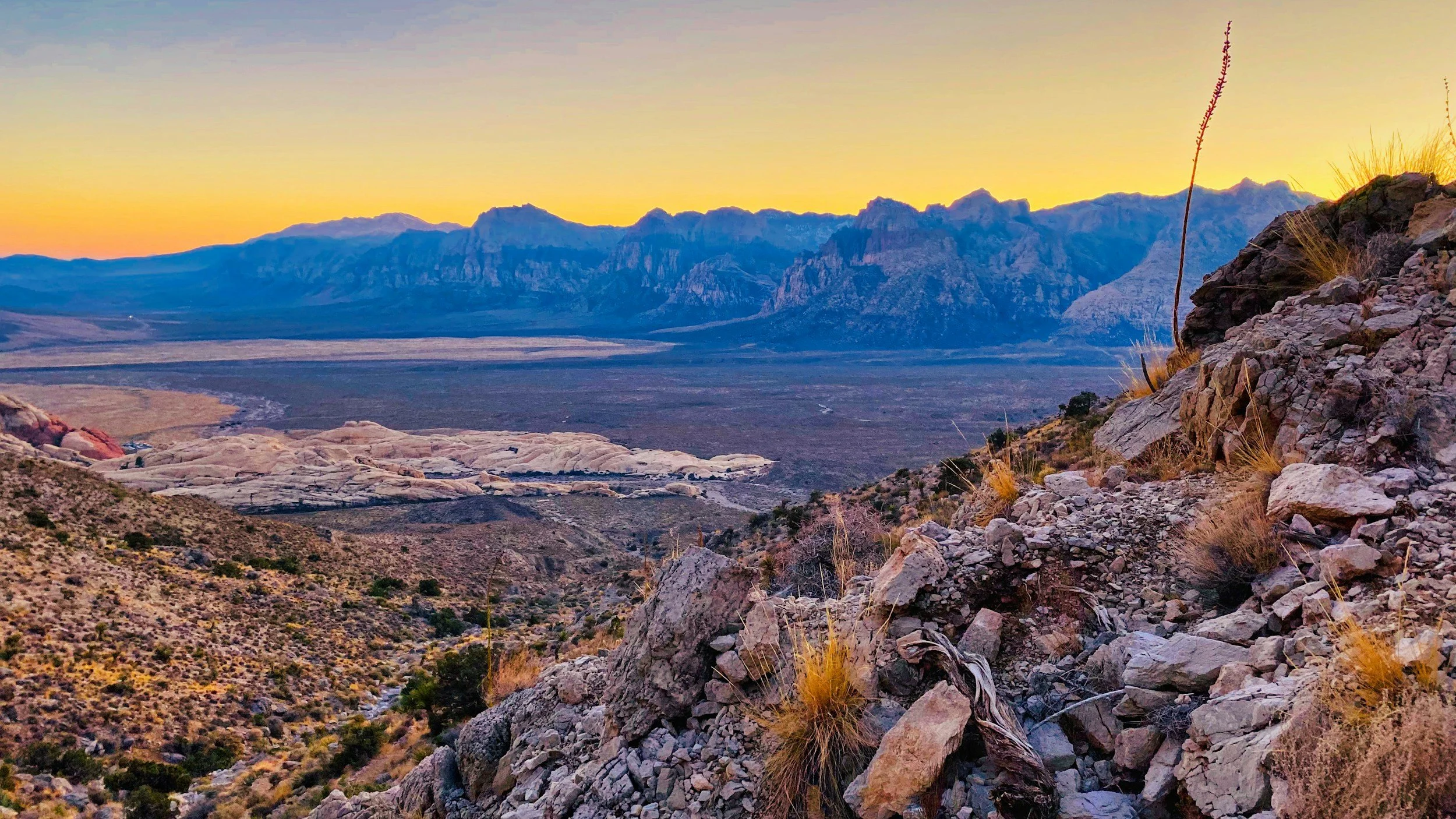 Scenic view of rocky desert terrain with mountains in the distance during sunset or sunrise.