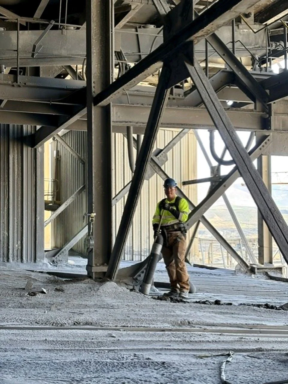 Prime Industrial worker in Northern Nevada wearing safety gear holding large pipe, standing inside a steel structure under construction.