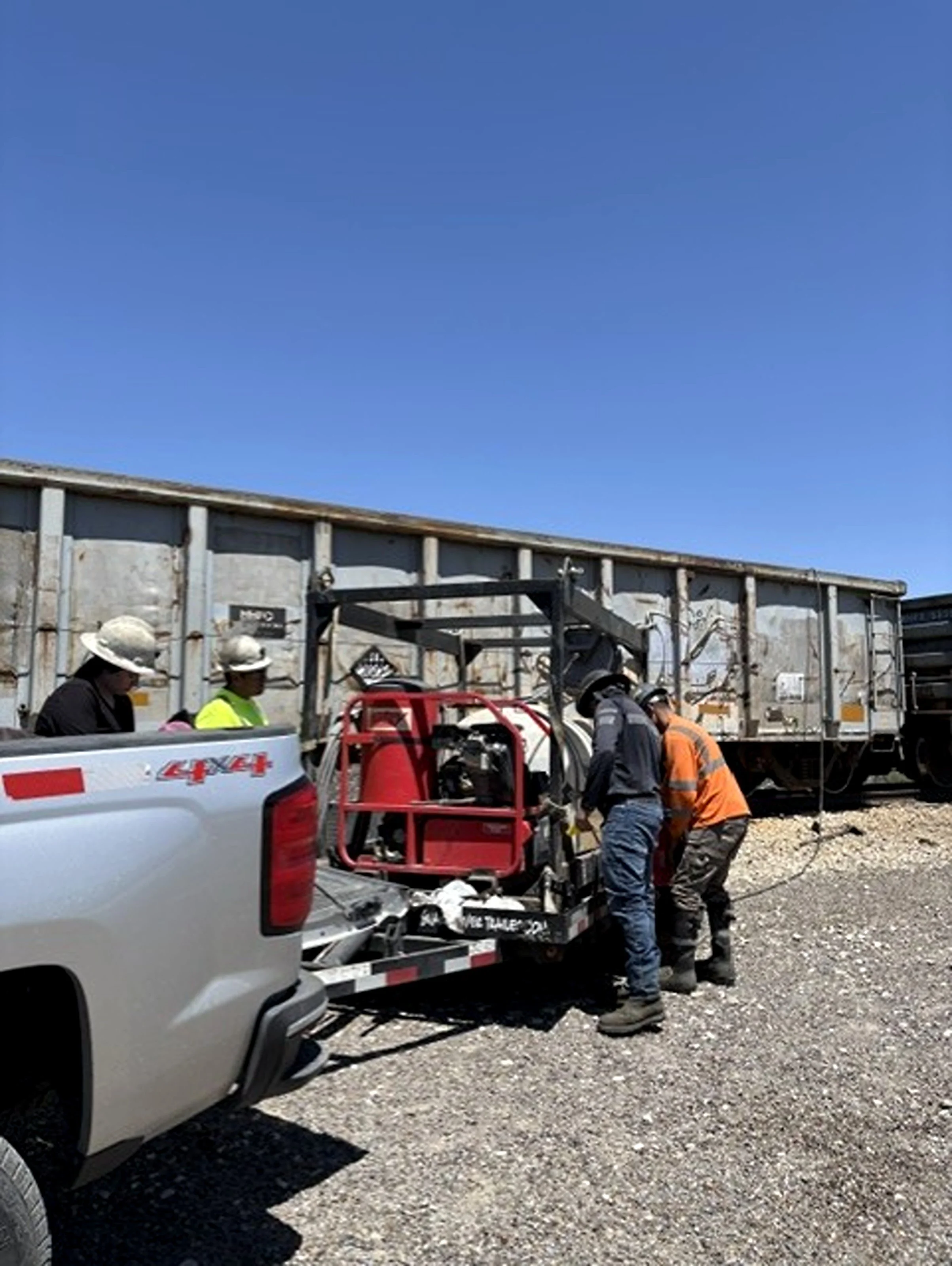 Construction workers wearing hard hats and safety gear working on a construction site with a truck and a blue sky.