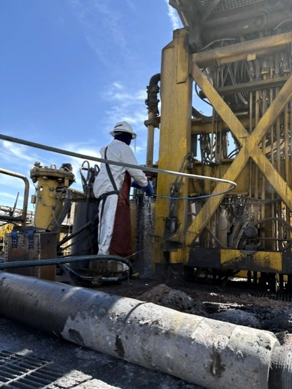 Worker in safety gear operating drilling equipment on an oil rig outdoors under a blue sky.