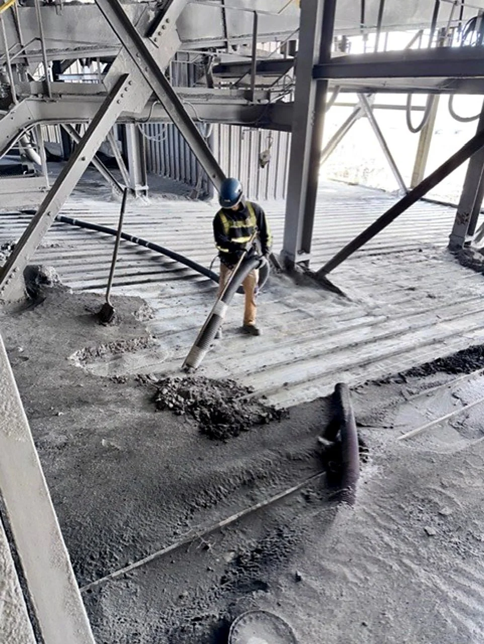 A construction worker is laying concrete floor at a construction site, using a large hose to pour concrete over the surface.