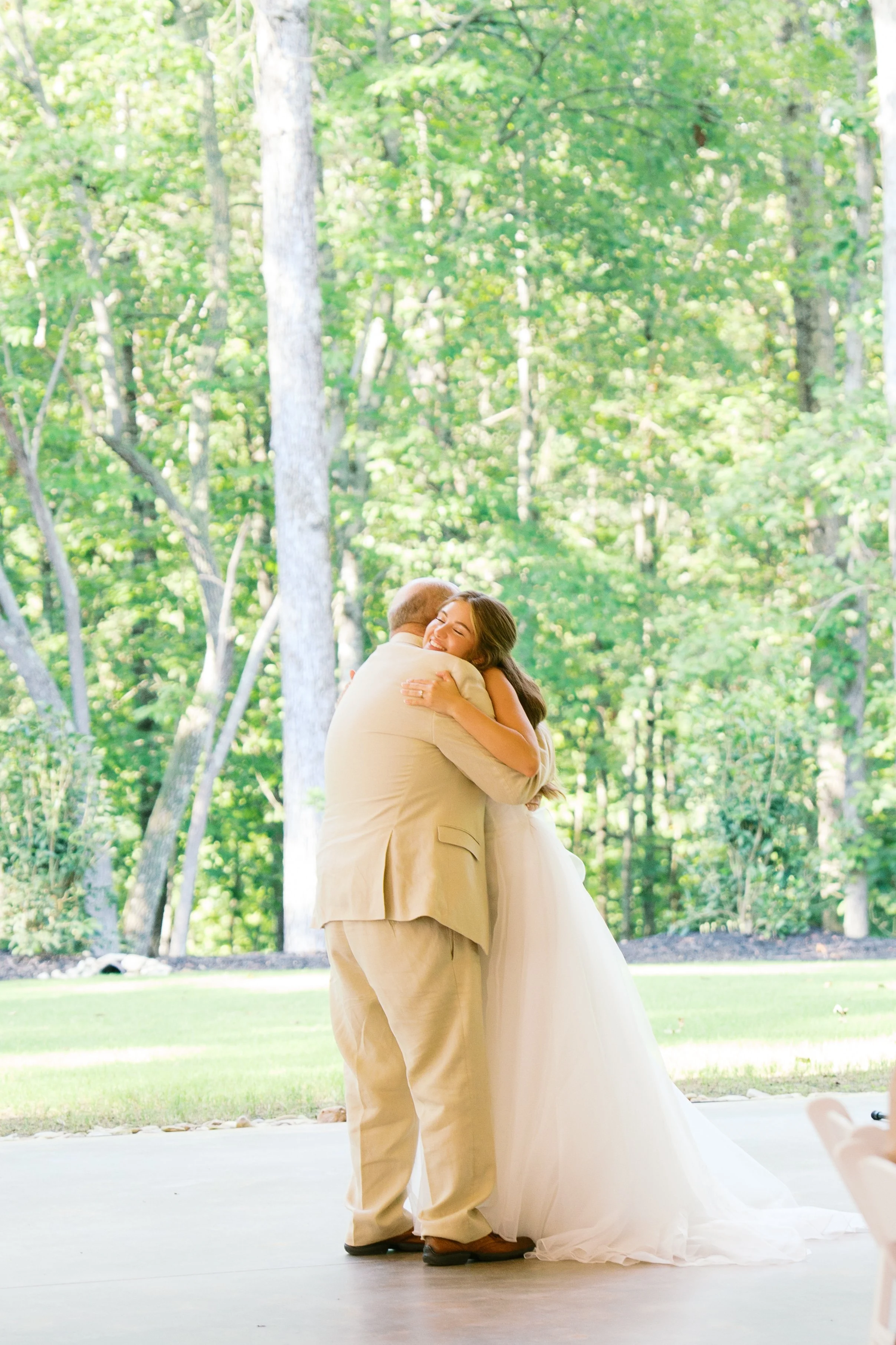 A couple hugging during their wedding ceremony outdoors in a green, wooded area.