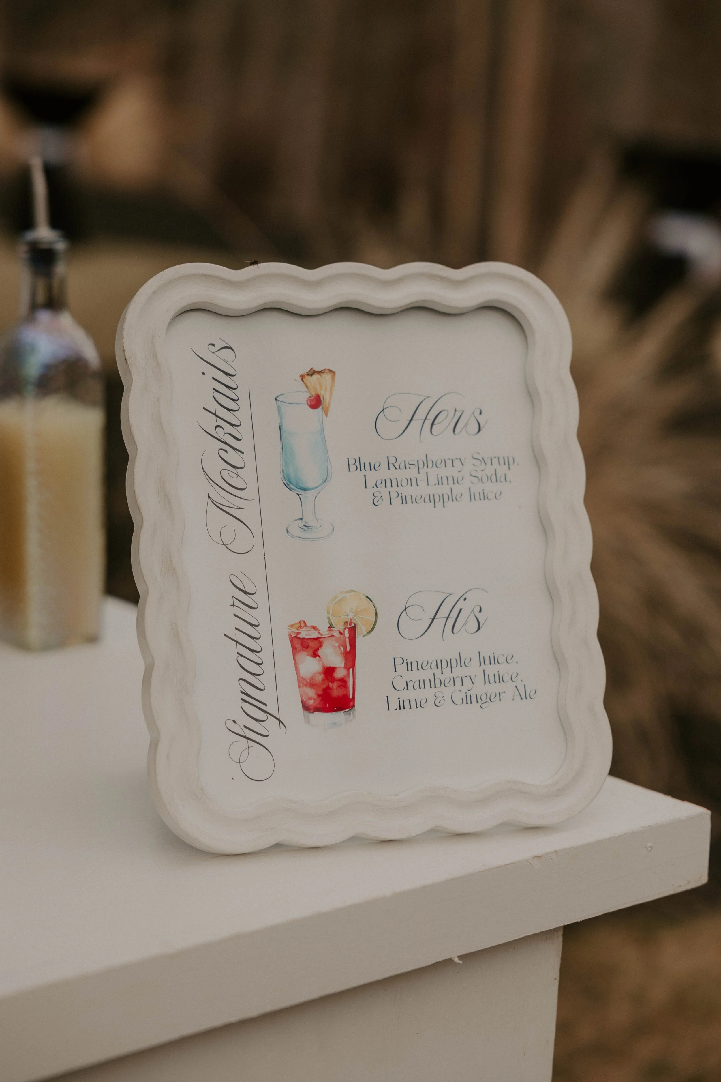 A decorative sign listing summer cocktails, including a blue raspberry syrup, lemon-lime soda, pineapple juice, cranberry juice, lime, and ginger ale, with watercolor illustrations of drinks.