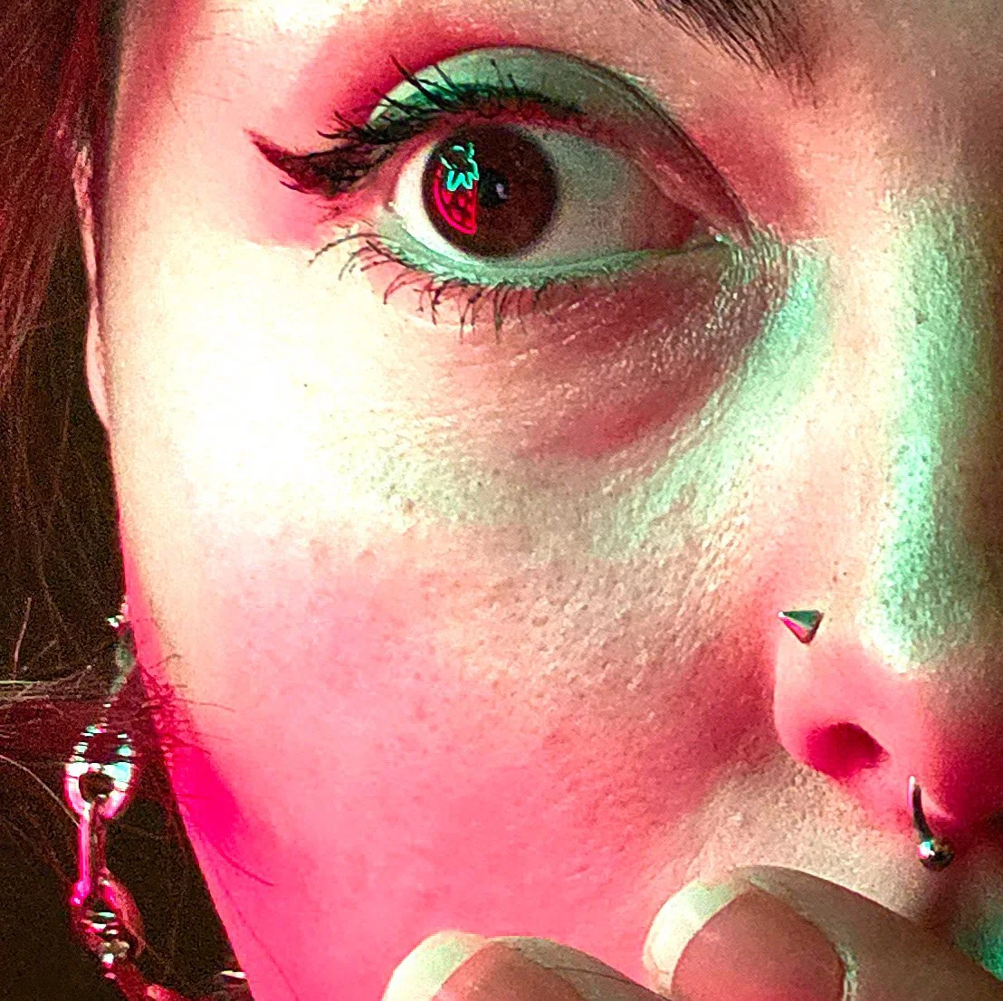 Close-up of a person's face with colorful makeup, nose piercing, and earrings.