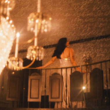A woman in a gown on a balcony overlooking a chandelier and ornate ceiling with written text.